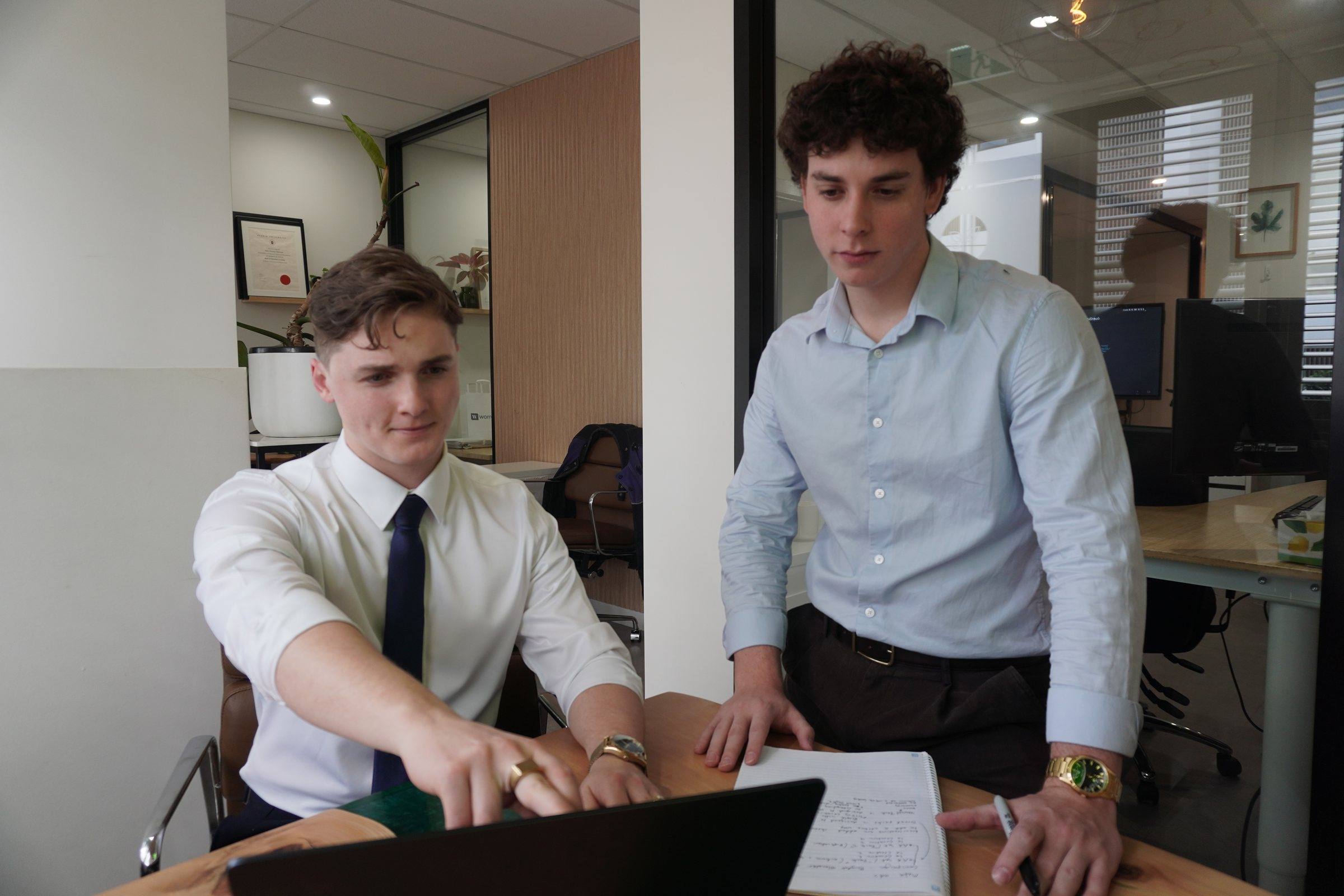 Zeek points at something on a laptop while Levi leans over to look